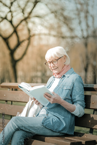 Ravishing elderly missis wearing glasses enjoying a book