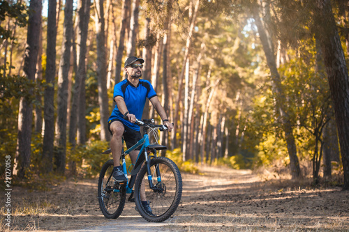 Happy bearded man cyclist rides in the sunny forest on a mountain bike. Adventure travel.