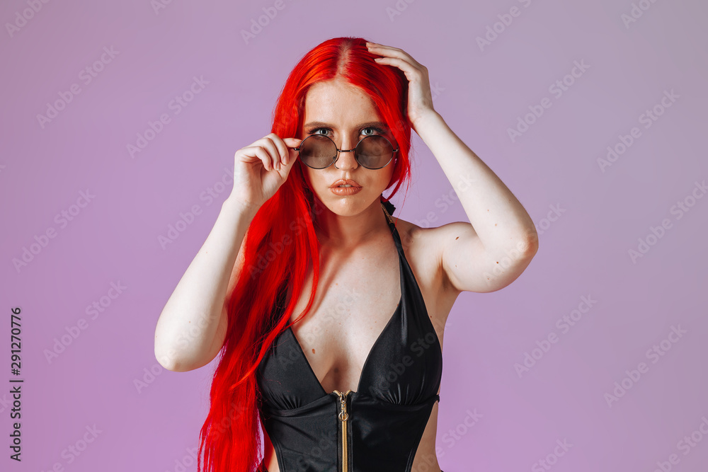 Portrait of a girl with red long hair in round glasses on a pink background Portrait of a girl with red long hair in round glasses on a pink background