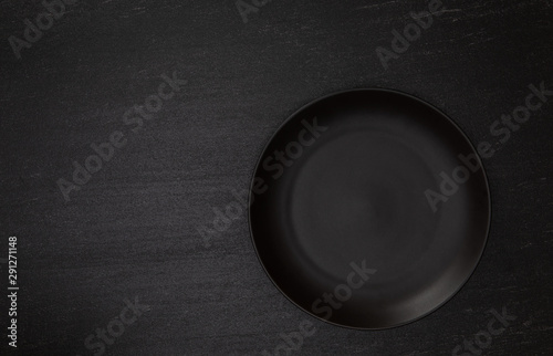 Empty blank black ceramic round plate or dish on black stone blackground with copy space, Top view of traditional handcrafted kitchenware concept