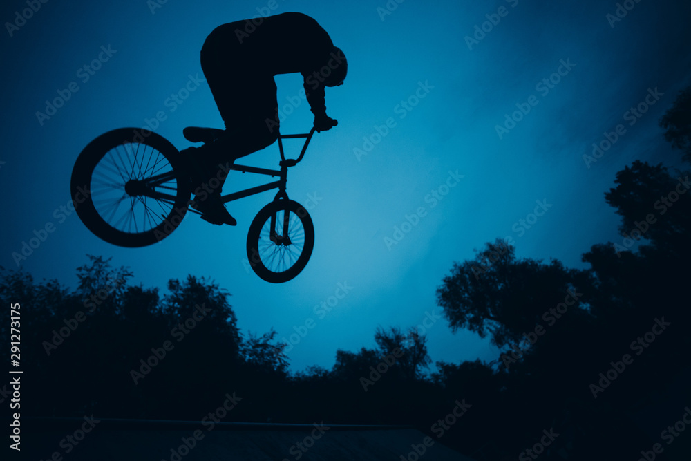 Naklejka premium Silhouette of professional young sportsman cyclist with bmx bike jumping at skatepark