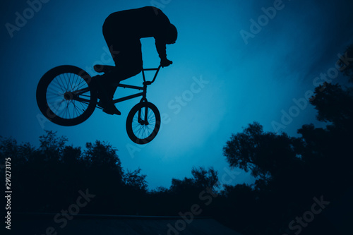 Photography Silhouette of professional young sportsman cyclist with bmx bike jumping at skat