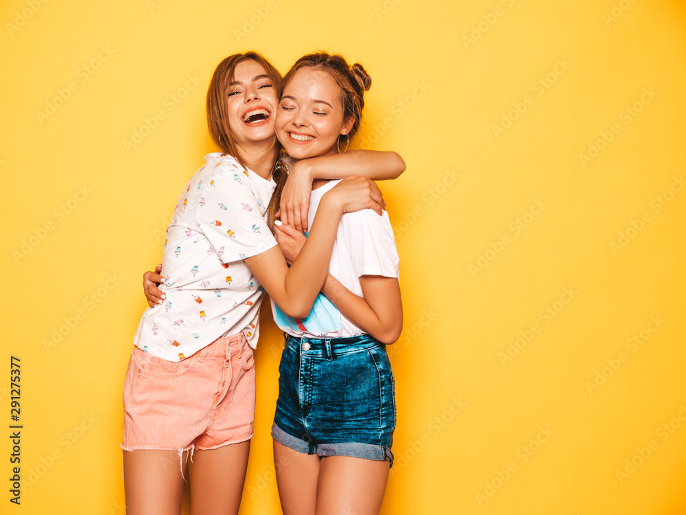 Two young beautiful smiling hipster girls in trendy summer clothes. Sexy carefree women posing near yellow wall in studio. Positive models going crazy and having fun.Hugging Two young beautiful smiling hipster girls in trendy summer clothes. Sexy carefree women posing near yellow wall in studio. Positive models going crazy and having fun.Hugging