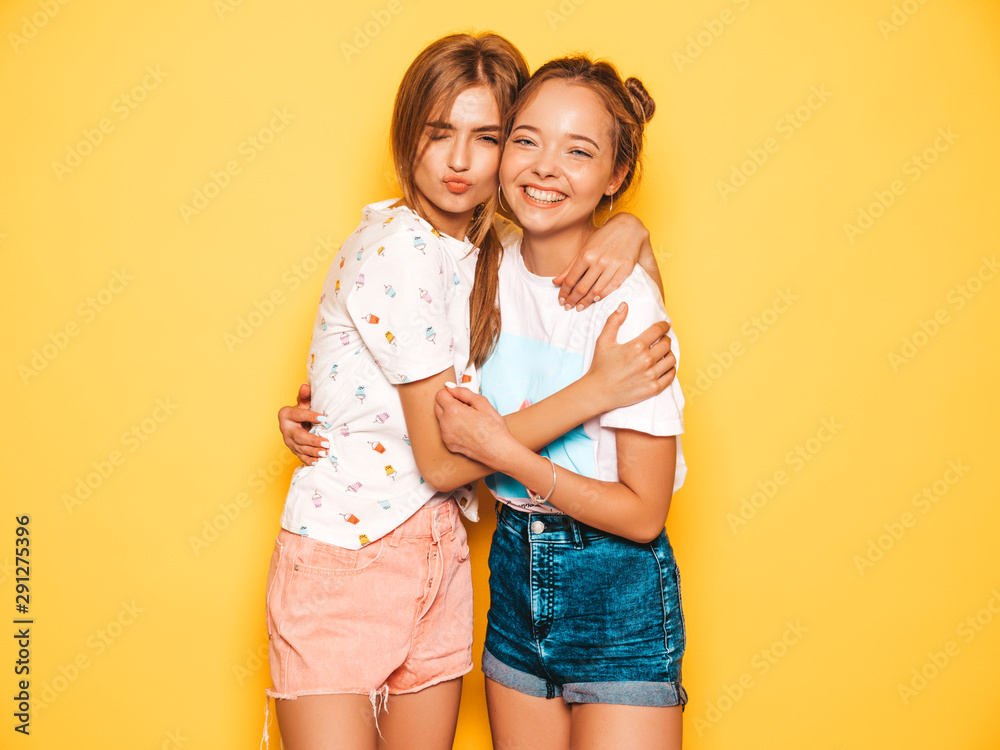 Two young beautiful smiling hipster girls in trendy summer clothes. Sexy carefree women posing near yellow wall in studio. Positive models going crazy and having fun.Hugging Two young beautiful smiling hipster girls in trendy summer clothes. Sexy carefree women posing near yellow wall in studio. Positive models going crazy and having fun.Hugging