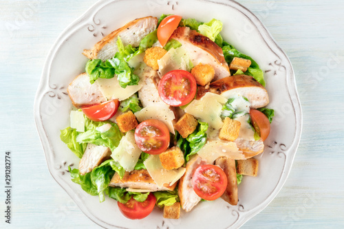 Caesar salad close-up. Slices of chicken breast, green lettuce, Parmesan cheese, croutons, and cherry tomatoes, shot from the top with the typical dressing