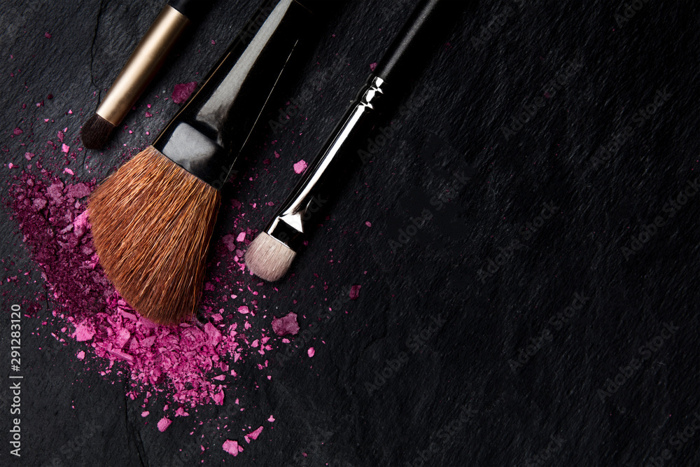 Make-up brushes with crushed cosmetics, shot from above on a black background with copyspace, a beauty design template for a makeup banner - obrazy, fototapety, plakaty 