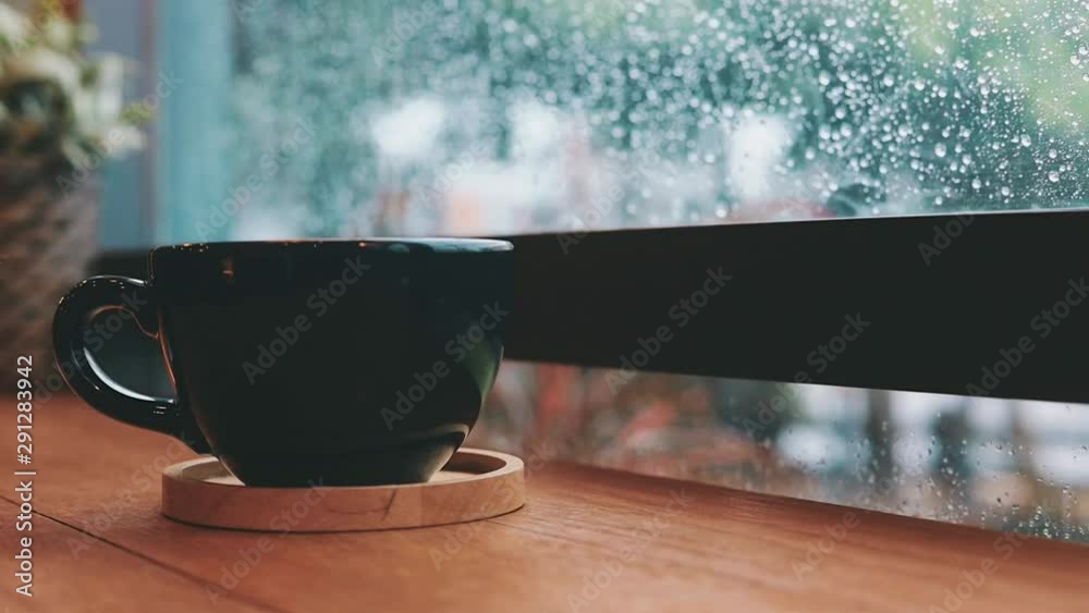 Hot coffee cup on table by the window in rainy day.