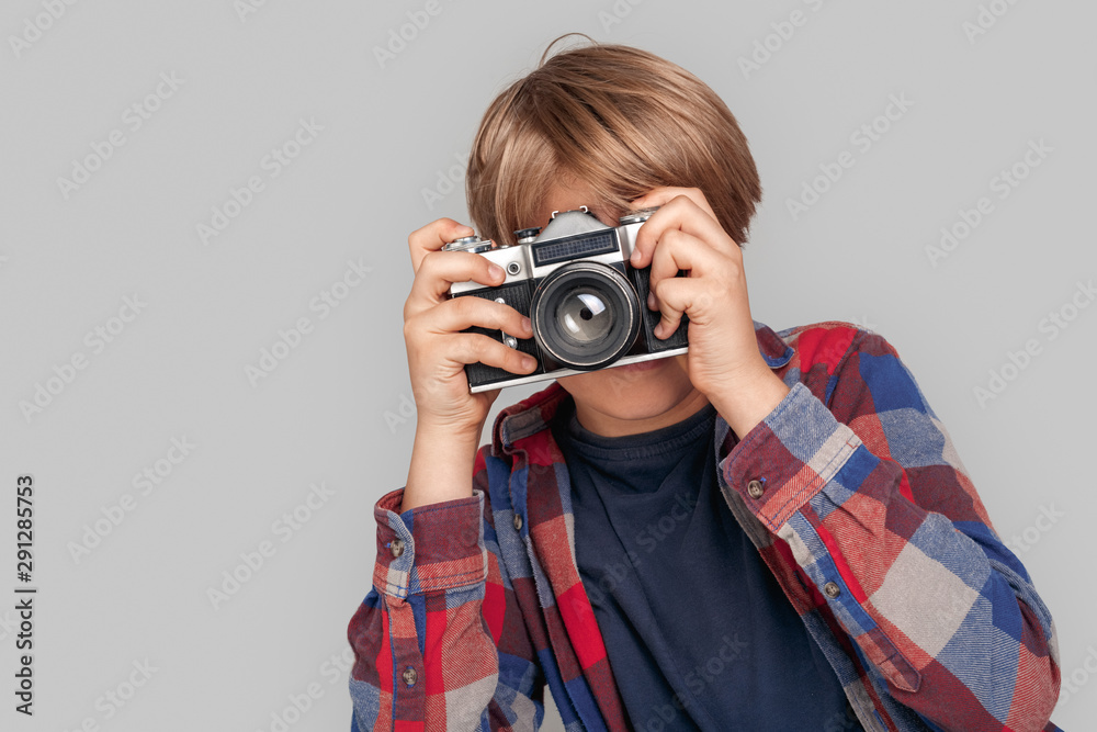 Freestyle. Young boy standing isolated on grey taking photo with camera Freestyle. Young boy standing isolated on grey taking photo with camera
