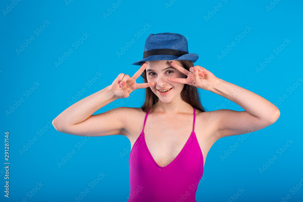 Young woman in lilac swimsuit lingerie and hat with hand gestures isolated on blue background Young woman in lilac swimsuit lingerie and hat with hand gestures isolated on blue background