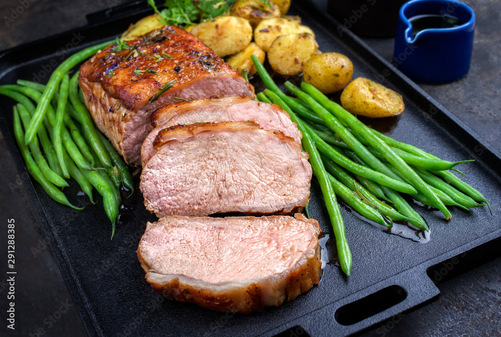 Traditional roasted dry aged veal tenderloin with beans and potatoes offered as closeup on a modern design cast iron tray