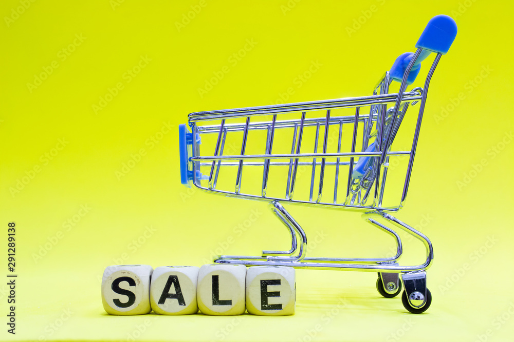 SALE-on wooden blocks with empty supermarket shopping cart on yellow background.