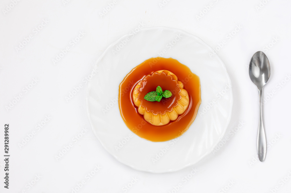 Flan or caramel custard pudding with spoon and mint on white plate over white background. Homemade Egg dessert. Top view Flan or caramel custard pudding with spoon and mint on white plate over white background. Homemade Egg dessert. Top view