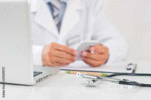 Senior doctor at his office in hospital working close-up using laptop holding smartphone