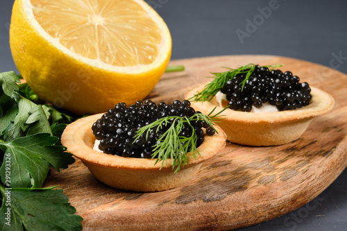 tartlets with red and black caviar on a wooden board with lemon and herbs on a gray background. Close-up