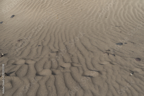 Dry sand gracefully laid with strong wind strips stretching into the distance and horizontal line of human traces swept up by the wind