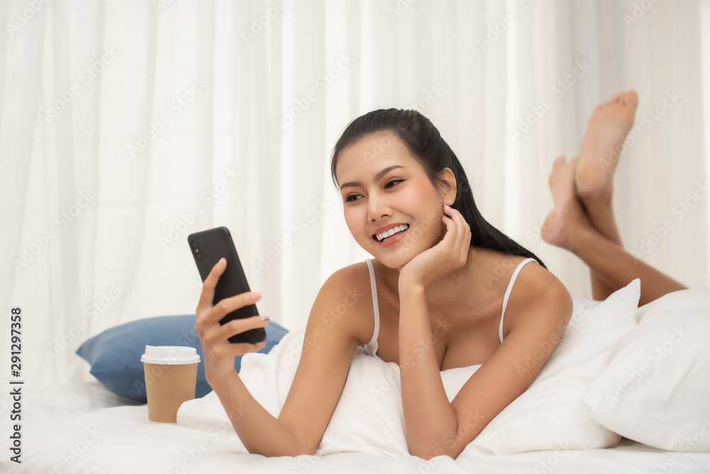 Young Woman Using Mobile Phone While Lying On Bed At Home Young Woman Using Mobile Phone While Lying On Bed At Home