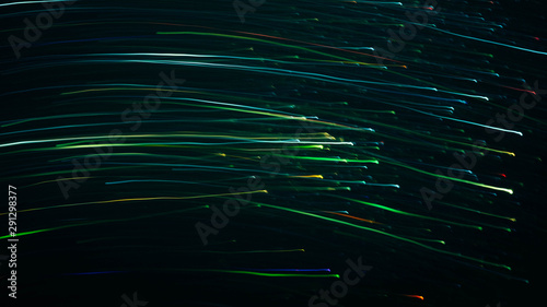 Blur multicolor flowing lights. Defocused neon green and blue illuminated lines and sparkles. Dark abstract background.