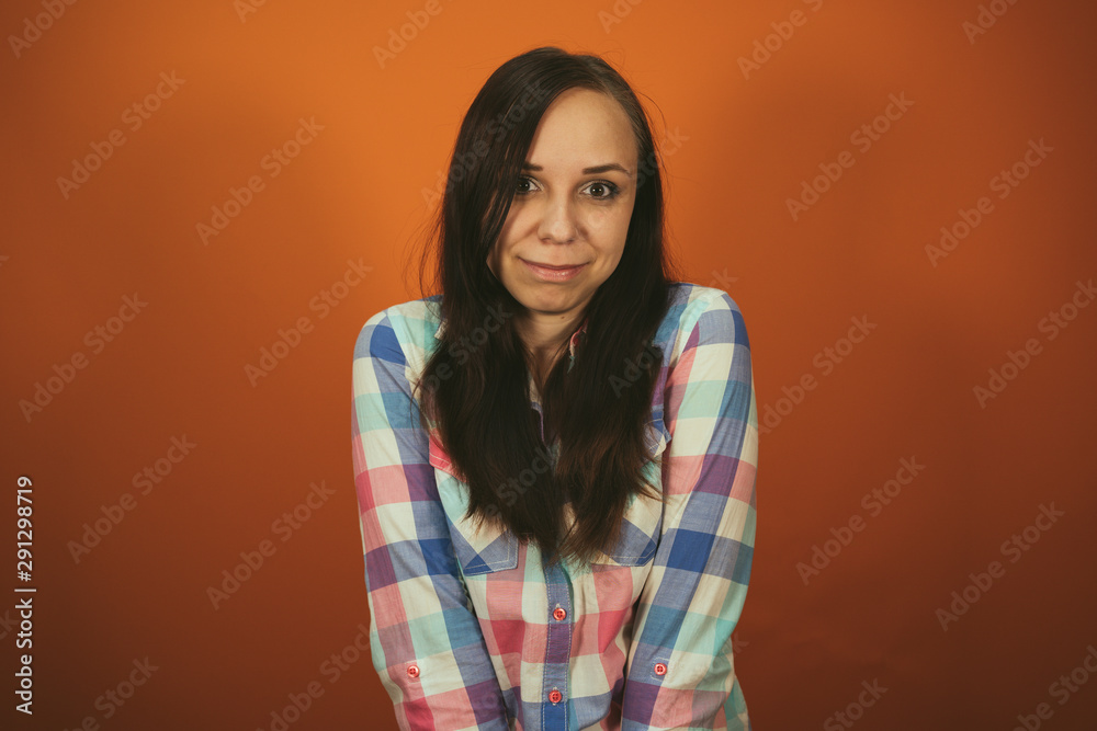 Fototapeta premium A beautiful woman in a plaid shirt poses on an orange background.