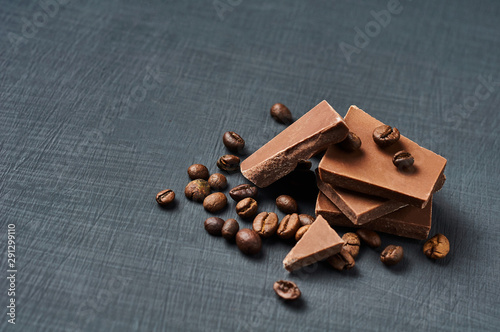 Heap of broken pieces of bitter or milk chocolate with fried coffee beans scattered on dark scratched concrete table. Space for text