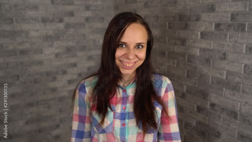 A beautiful young woman in a plaid shirt is aping on a gray brick background. A beautiful young woman in a plaid shirt is aping on a gray brick background.