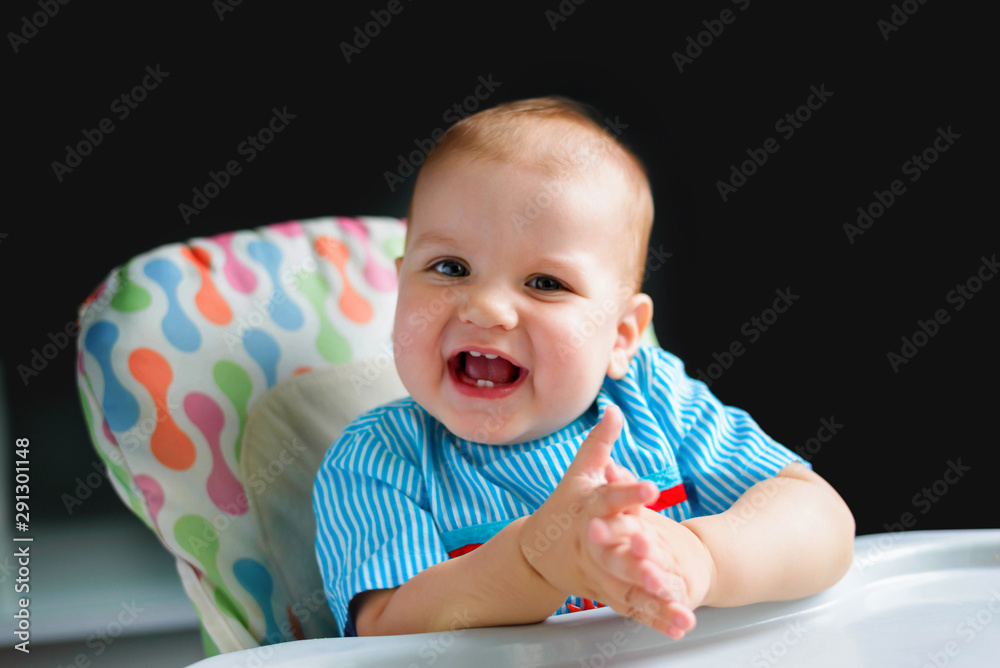 Funny kid boy 10 months old sitting in a baby chair for feeding in the kitchen at home. Baby food concept. Funny kid boy 10 months old sitting in a baby chair for feeding in the kitchen at home. Baby food concept.