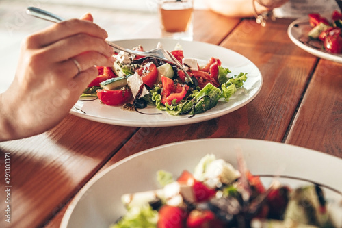 Girl eats popular greek vegetable salad with feta cheese and herbs. Plate with salad on the wooden table in the restaurant. Close up photo of girl with fork in her hands.