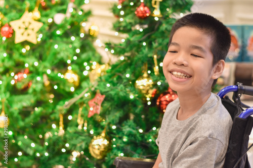Asian special child on wheelchair smiling as happily with blurred lighting, Christmas Festival background, Life in the education age of disabled children, Happy disabled kid concept.