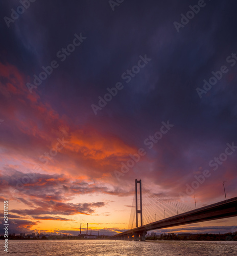 Beautiful dusk landscape with bridge over river Dnipro. Dramatic colorful sky.