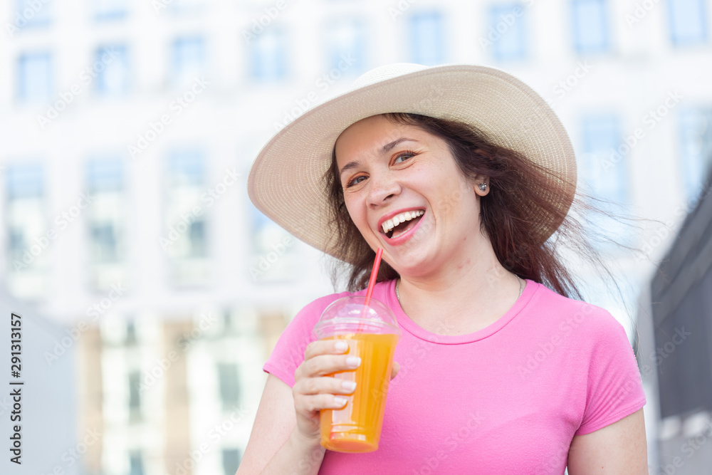 Φωτογραφία Bottom view portrait of a young beautiful cheerful woman in a hat walking around the city with juice on a warm summer day