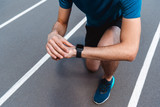 partial view of athletic young sportsman looking at smartwatch on running track