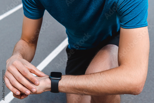 cropped view of athletic young sportsman showing smartwatch on running track