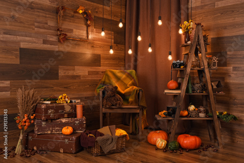 Beautiful vintage autumn composition with pumpkins, teddy bear, magic lights, cozy plaid and old suitcases. Fall season. Thanksgiving and Halloween concept.