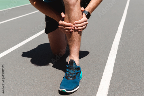 cropped view of athletic young sportsman touching leg on running track
