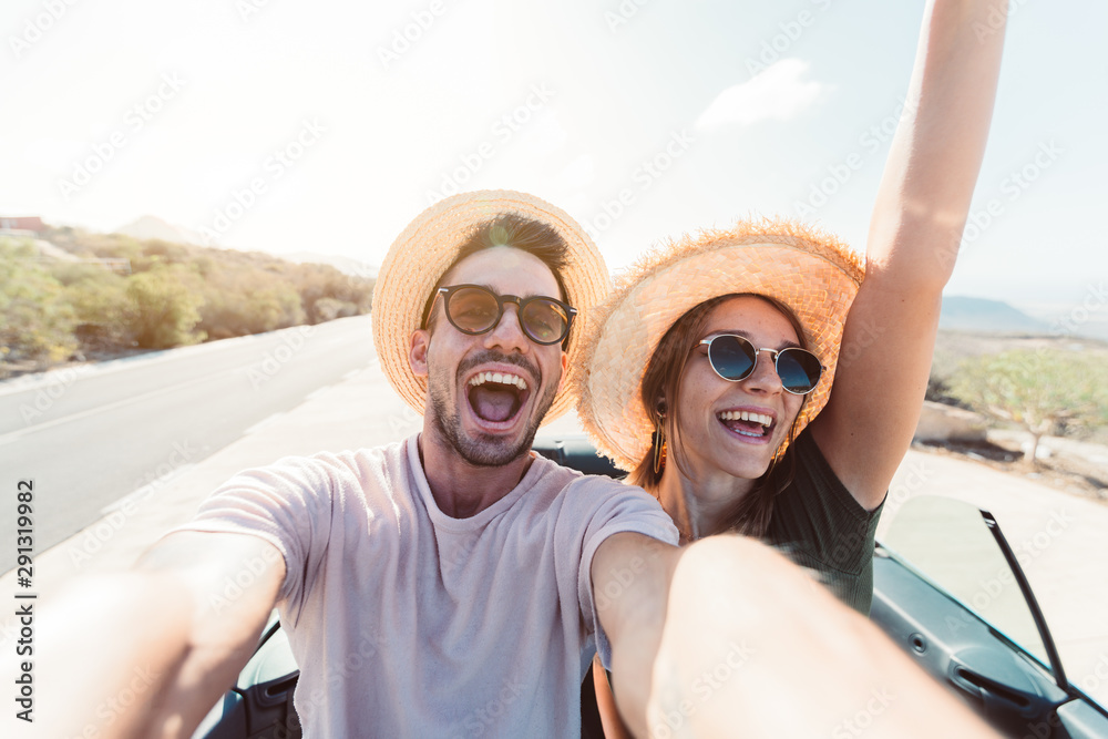 Happy couple in love taking a selfie when road trip in a convertible car - obrazy, fototapety, plakaty 