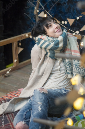 Beautiful girl in a warm scarf against the background of a minimalist Scandinavian interior and garlands, Christmas and New Year concept, selective focus