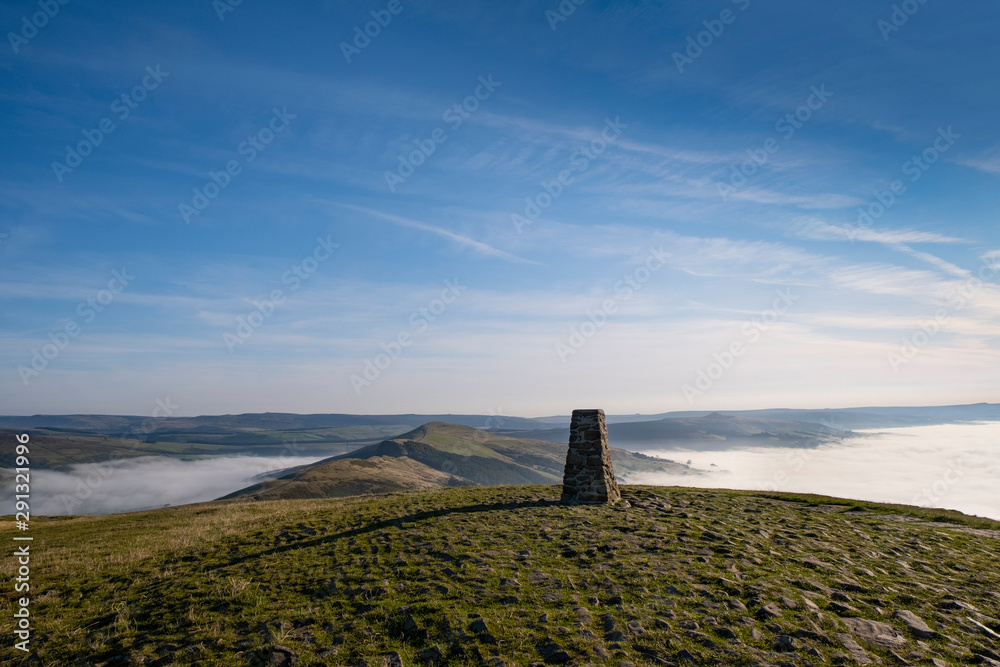 Trig point on top of Mam Tor, Peak District, UK. Early morning with mist in Edale and Hope Valley, and the Great Ridge rising above the mist