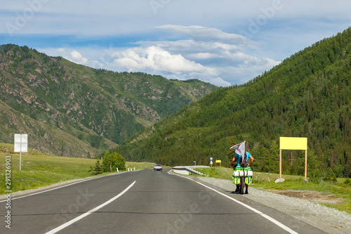 A strong man in helmet ride on sport bicycle with bags on a road in the mountains of the Altai climbing up by highway in autumn indian summer. Travelling and trip around the world.