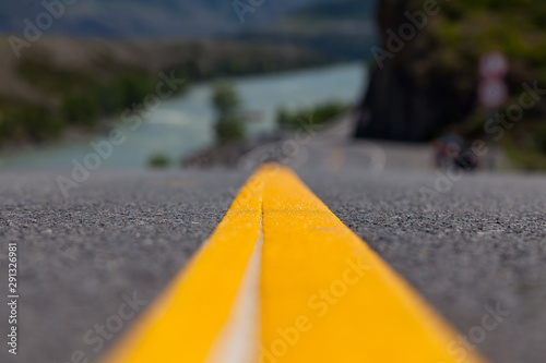 Close-up on a yellow dividing strip on an asphalt road stretching into the Altai Mountains near a rock with rocks and a river with a picturesque landscape in the background
