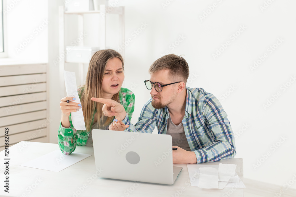Young husband and wife are upset about numerous checks for payments and purchases for repairs while sitting at the table with a laptop. The concept of low living standards and savings. Young husband and wife are upset about numerous checks for payments and purchases for repairs while sitting at the table with a laptop. The concept of low living standards and savings.