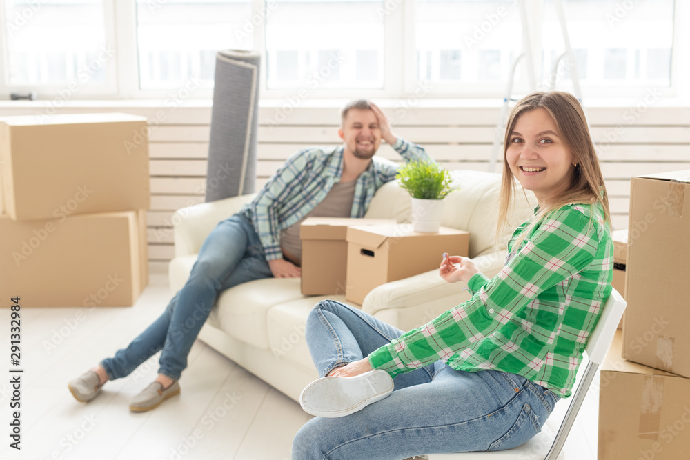 Positive cheerful couple rejoices in moving their new apartment sitting in the living room with their belongings. Concept of housewarming and mortgages for a young family. Positive cheerful couple rejoices in moving their new apartment sitting in the living room with their belongings. Concept of housewarming and mortgages for a young family.