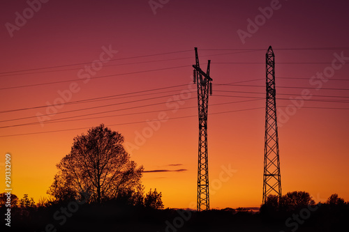 High voltage electricity transmission pylons against sunset and tree silhouettes