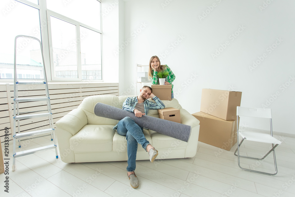 Satisfied cheerful young couple strong man and pretty woman holding their things in their hands sitting in the living room of a new apartment. Housewarming concept. Satisfied cheerful young couple strong man and pretty woman holding their things in their hands sitting in the living room of a new apartment. Housewarming concept.