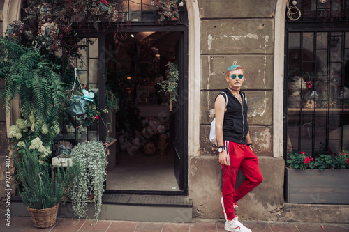 Homosexual male with stylish hairstyle and gay glasses posing at flowers boutique on background © benevolente