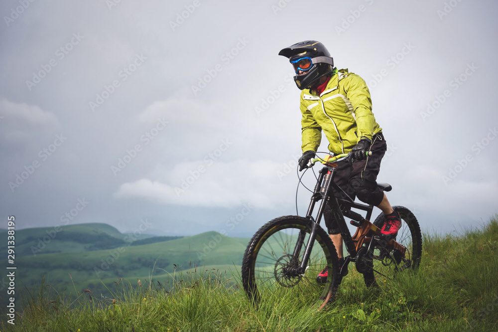 Front view of a man on a mountain bike standing on a rocky terrain and looking down against a gray sky. The concept of a mountain bike and mtb downhill Front view of a man on a mountain bike standing on a rocky terrain and looking down against a gray sky. The concept of a mountain bike and mtb downhill