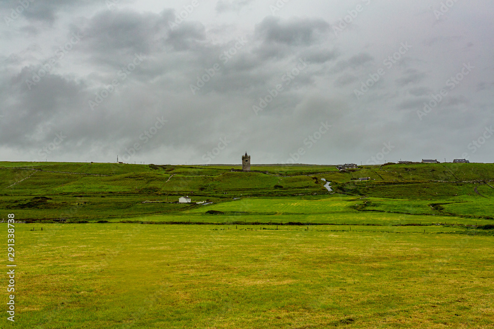 Obraz premium Beautiful landscape of the Irish countryside with the castle Doonagore in the background in the village of Doolin, Wild Atlantic Way, cloudy day in county Clare in Ireland