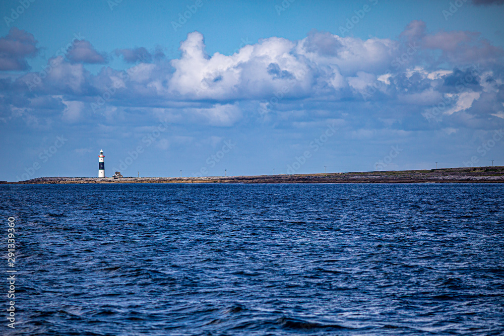 Lighthouse built in 1857 on the Inis Oirr island seen from a boat, wonderful sunny day with a blue sky and white clouds in the Aran Islands, Ireland