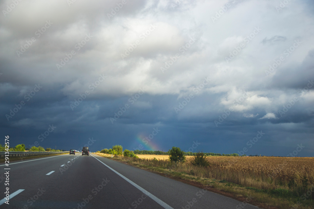 road and blue sky with small raibow on the field 