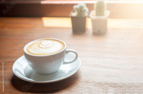 Hot coffee cup with latte art on the wooden table in the morning with sun shines through window.