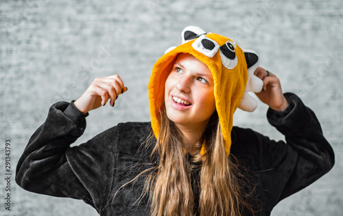 portrait of young teenager brunette girl with long hair dressed in a kigurumi pajamas costume on gray wall background photo