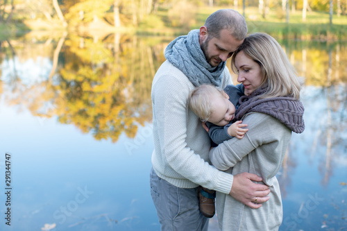 Loving family couple hugs their sleepy child at nature with lake on background.